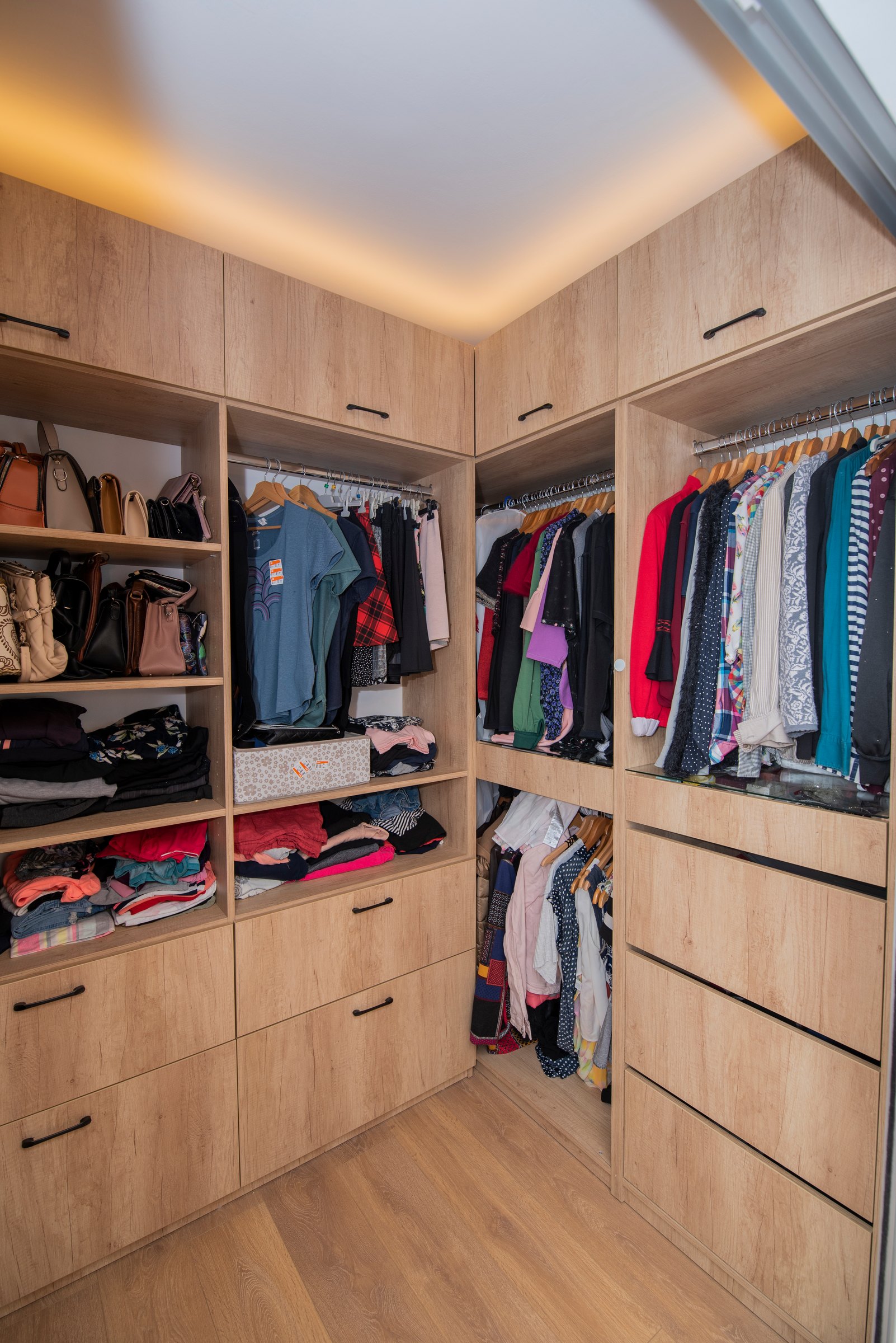 Colțul dressingului, cu lumină caldă la tavan și sertare în decor de stejar